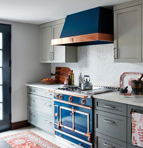 a deep blue kitchen stove with a copper touch and a matching hood in a grey kitchen