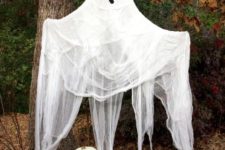 15 a large cheesecloth ghost with a spooky face and some pumpkins under it