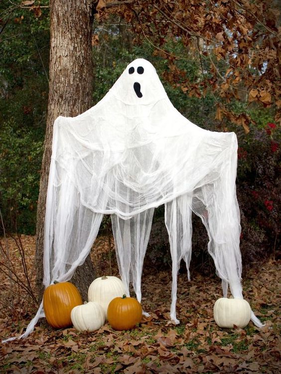 a large cheesecloth ghost with a spooky face and some pumpkins under it