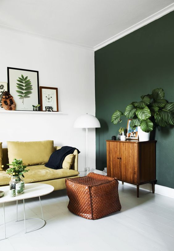 a dark green statement wall and a yellow sofa look organic and chic together