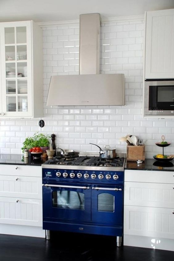 a traditional white kitchen is made eye-catchy with a subway tile backsplash and a cobalt blue cooker