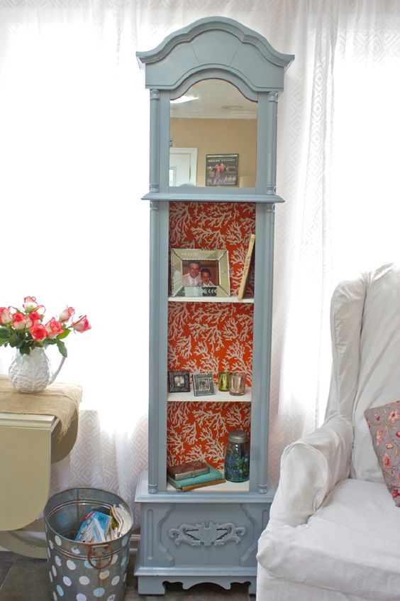a grandfather's clock repurposed into a shelf, a mirror attached and coral print wallpaper inside