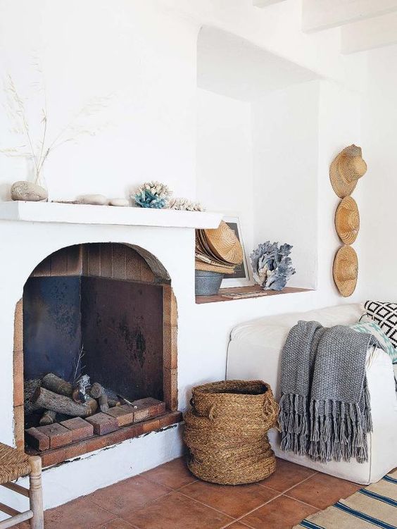 the mantel is decorated with corals, shells, pebbles and straw hats on the wall add to the decor
