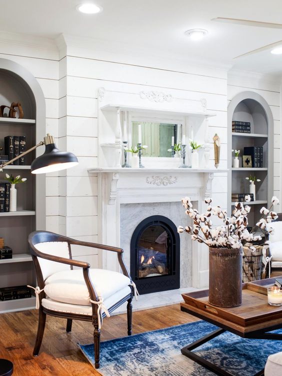 a vintage fireplace in white is used as a cover for a modern electric fireplace to add a cozy touch