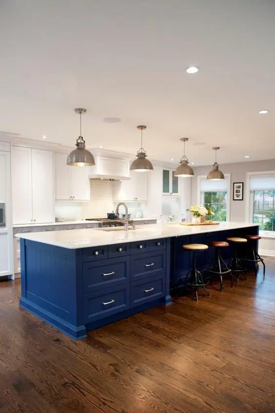 a white kitchen is spurced up with a large bold blue island, which is topped in white to connect to the space