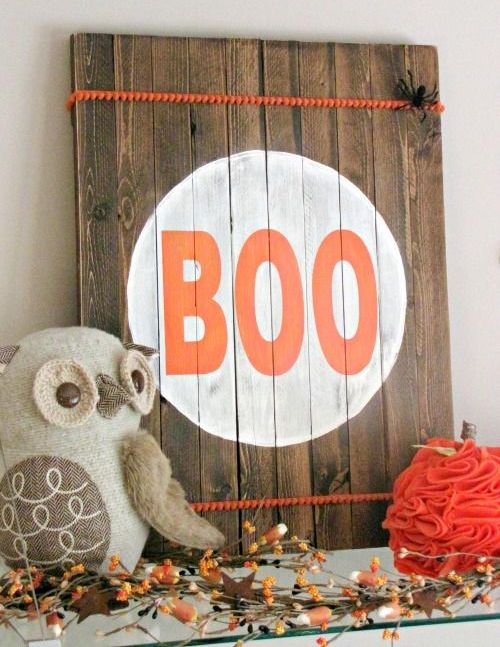 a pallet wooden sign with orange pompom trim, bold BOO letters and a couple of faux spiders