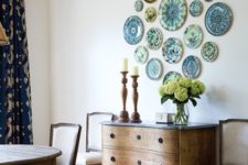 28 blue and green decorative plates styled on the wall of a dining room