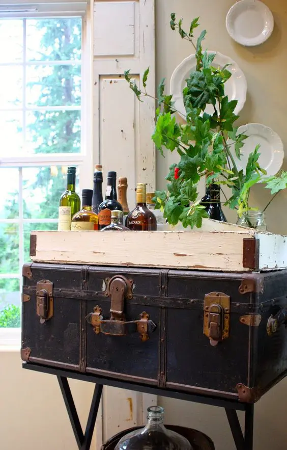 a vintage trunk placed on metal legs is used as a home bar