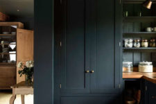 02 The cabinetry is black with brass handles, and warm wooden kitchne countertops contrast with this color