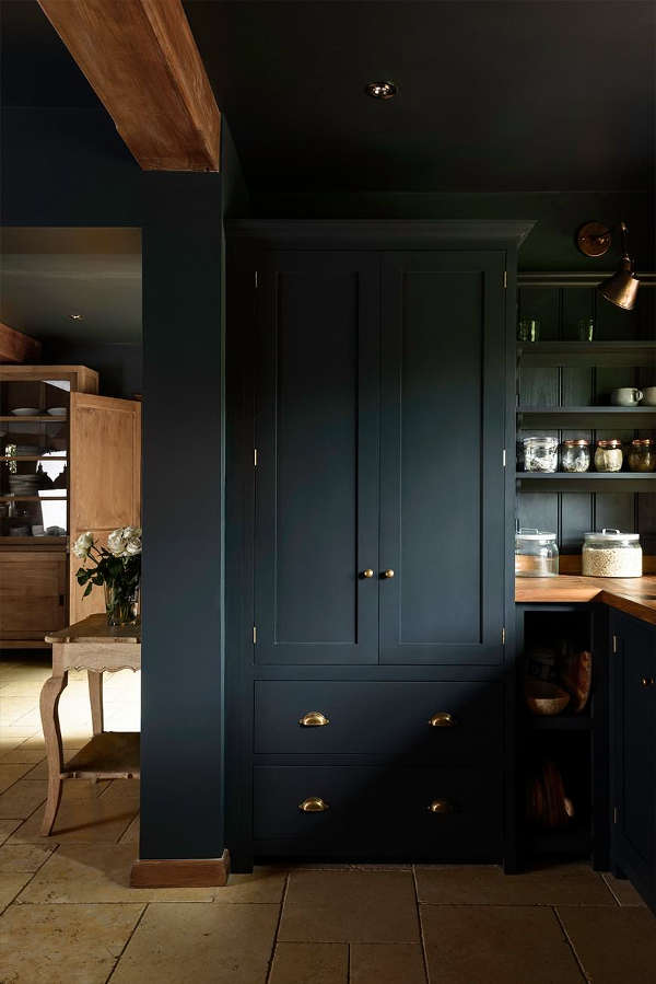 The cabinetry is black with brass handles, and warm wooden kitchne countertops contrast with this color