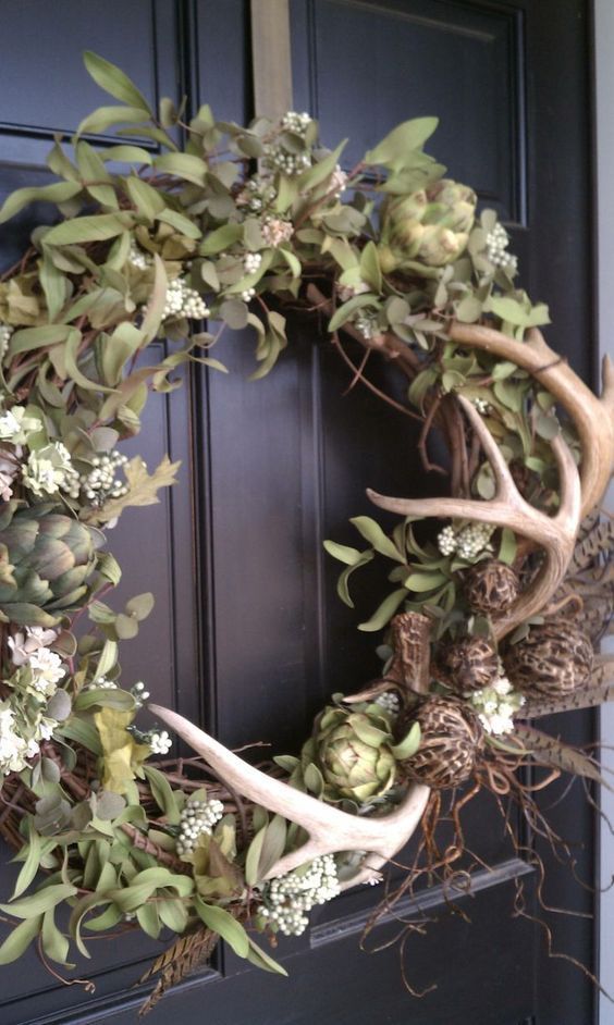 a cool fall wreath with greenery, artichokes, antlers and feathers is great and feels like woodlands