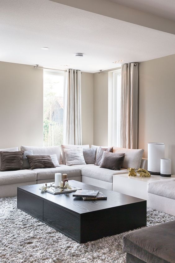 a modern clean space done in neutrals, with a black coffee table and brown pillows, soft curtains