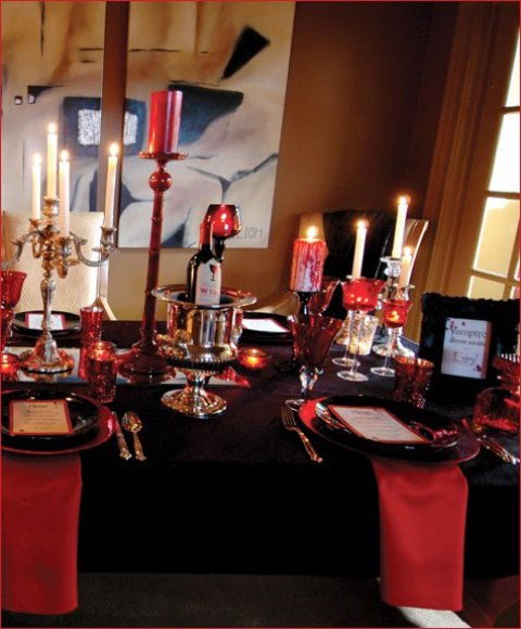 a black and deep red party table with red candles and candle holders, red napkins with a black tablecloth