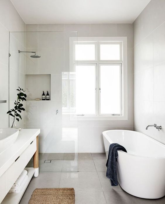 A modern neutral space with a seemless shower space, a free standing tub, vanity with open shelves and a jute rug