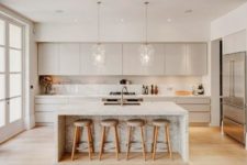 03 a neutral kitchen with cream cabinets, a white kitchen island with marble touches and pendant lamps