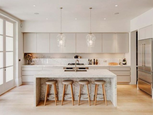 a neutral kitchen with cream cabinets, a white kitchen island with marble touches and pendant lamps