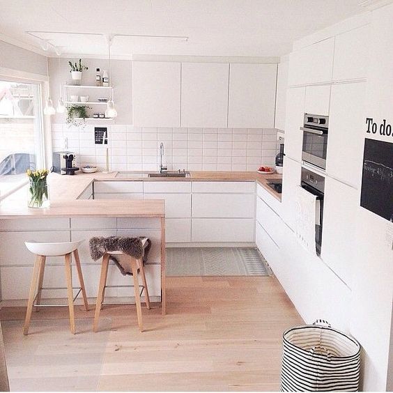 A small U shaped kitchen done in white with a breakfast space and cooking zone in one