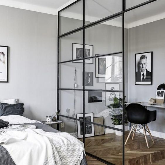a masculine bedroom and a workspace separated with a glazed framed wall