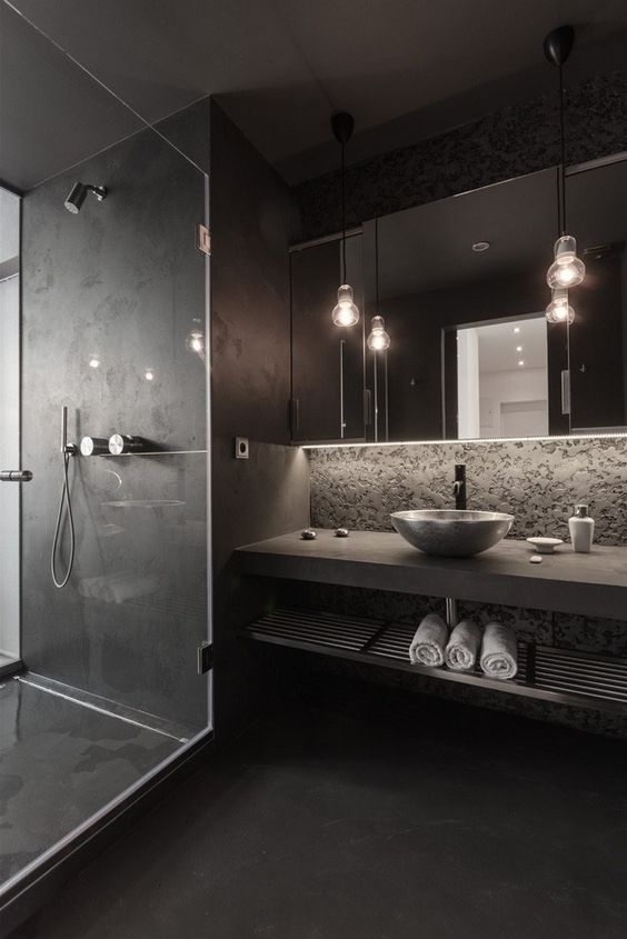 a modern moody space with a stone wall, a concrete vanity shelf, a matte black shower and floor