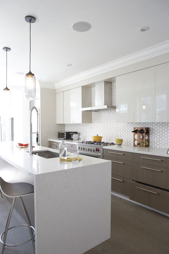 a modern space with sleek white cabinets and wooden ones, a geo tile backsplash and a marble kitchen island