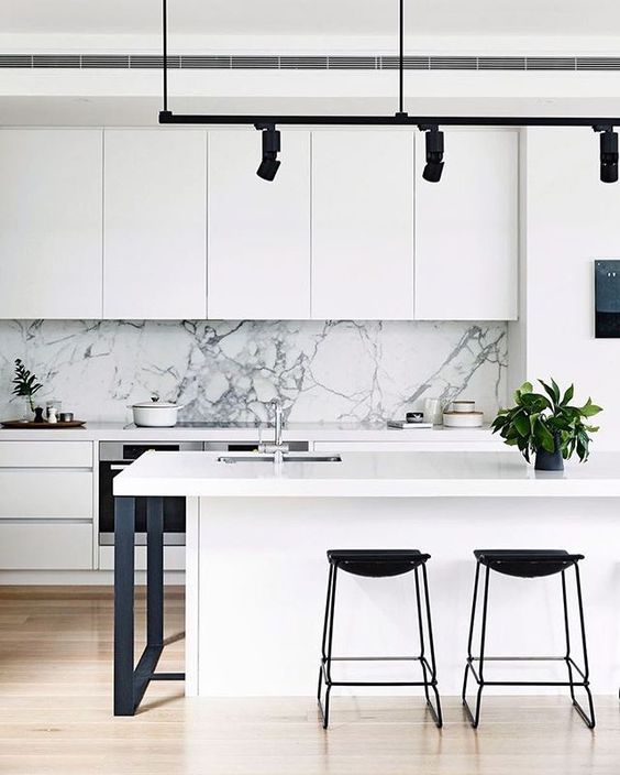 a white kitchen with a white marble backsplash and metal details for a cool look