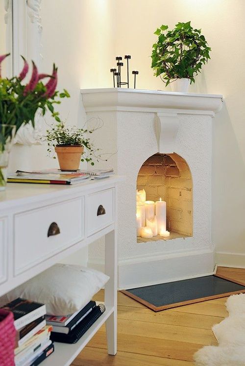 a whitewashed non-working fireplace features some candles, which make the space cozier and comfier