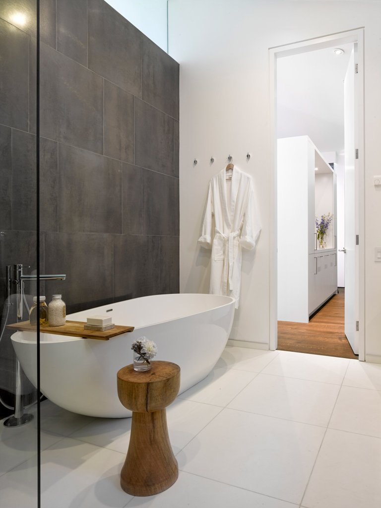 The master bathroom is done in white except for one accent wall clad with graphite grey tiles, and natural wood adds a spa touch
