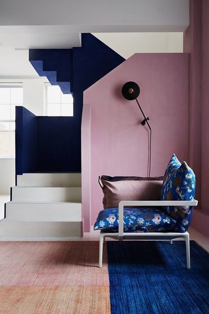 a gorgeous sculptural entryway with a dusty pink wall and navy and white staircase