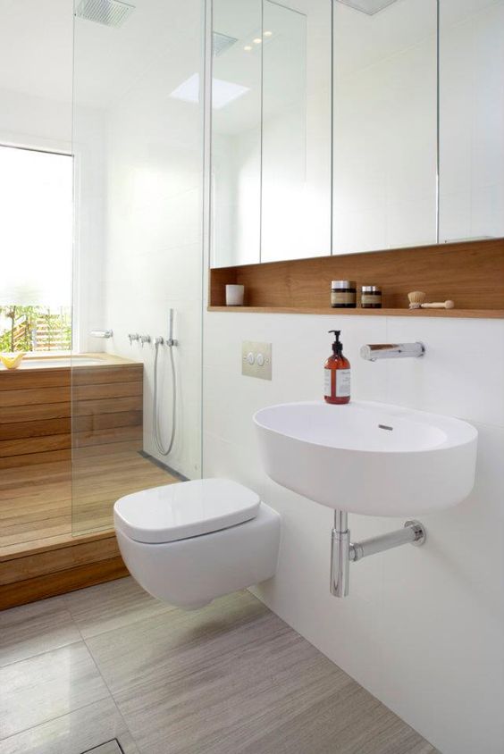 a white space with a wooden built-in shelf, a wood clad shower and bathtub and sleek white panels
