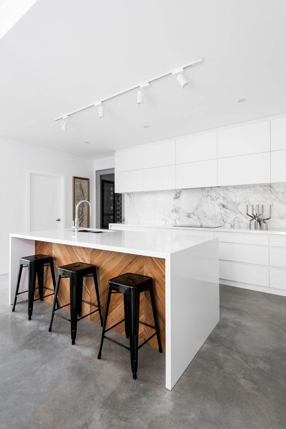 an all-white kitchen with a marble backsplash and a white kitchen island clad with wood