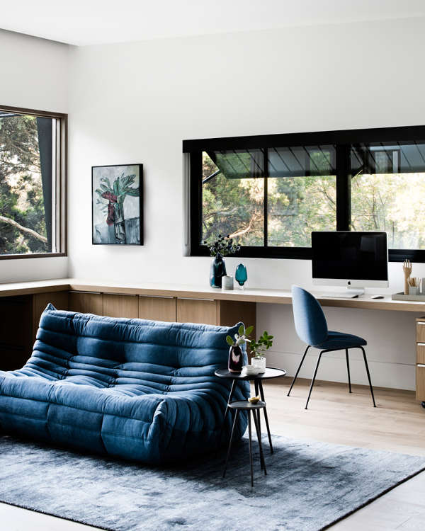 The home office is done with a long windowsill desk, a blue chair and a matching sofa