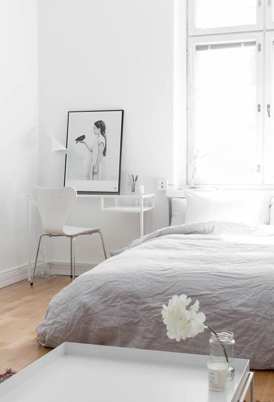 an airy neutral bedroom with a working space in the corner that may double as a makeup nook