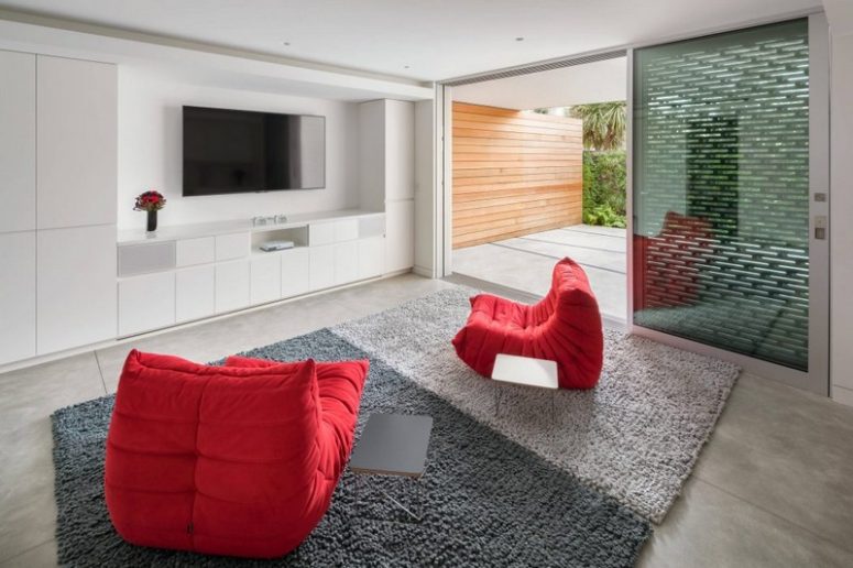 This space with a TV and red chairs is located next to a terrace, which is also kept private with screens