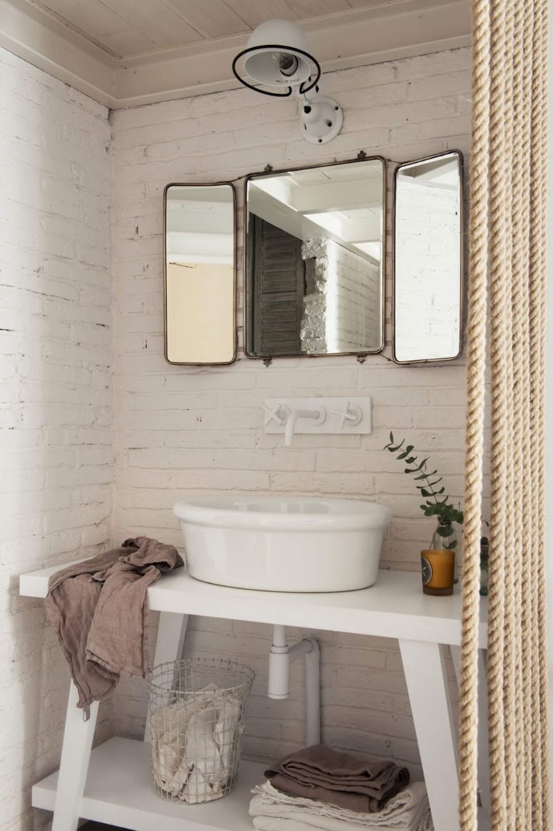 There's a powder room with white brickwork, a vintage sink and mirror and a rope curtain