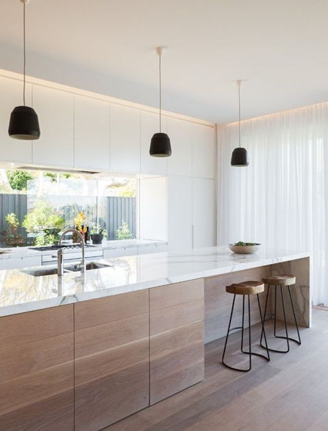 A modern light colored kitchen with a wooden kitchen island and marble counters