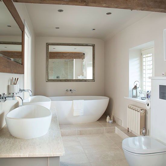 a modern soft-colored bathroom with a free-standing tub, white sinks and neutral tiles