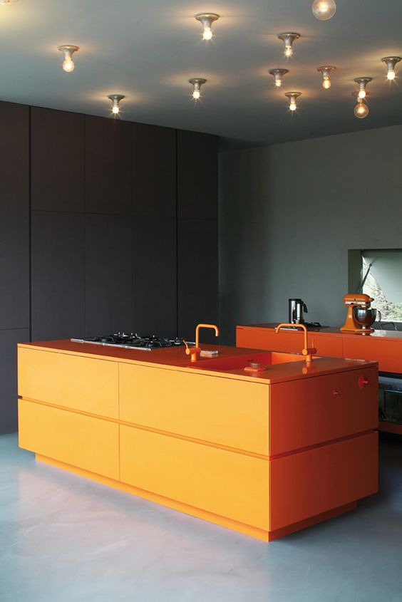 a moody kitchen with a bold orange kitchen island and cooking space to cheer it up