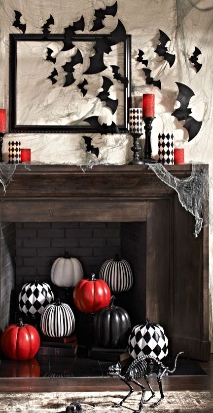 a stylish mantel with bats and red and checked candles and a fireplace filled with checked, striped and red pumpkins