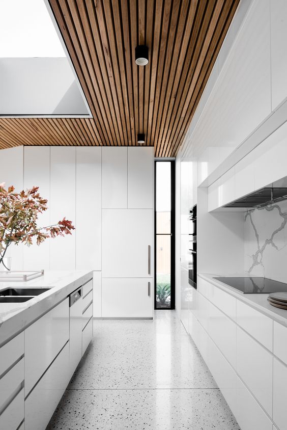 a modern all-white kitchen with a marble backsplash and a wooden ceiling
