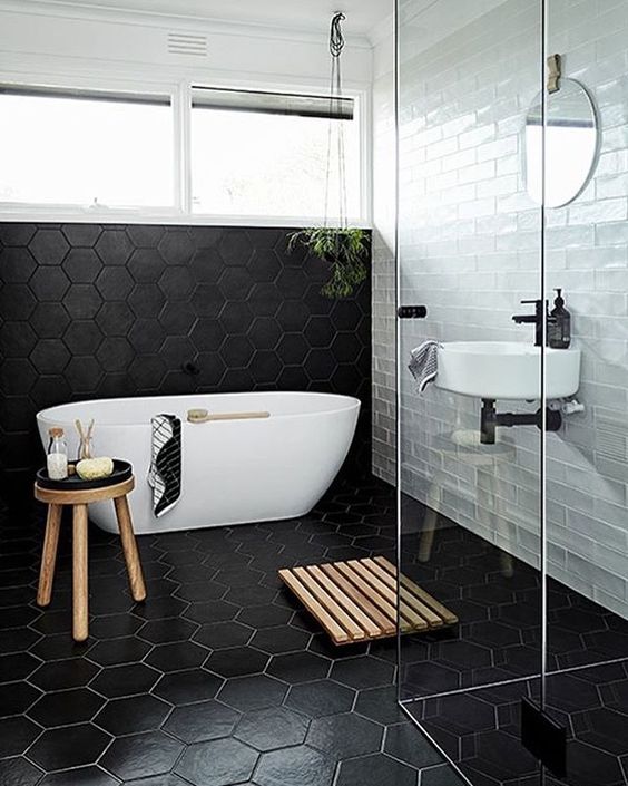 A modern space with subway tiles, black geo tiles, a free standing bathtub, some wooden touches