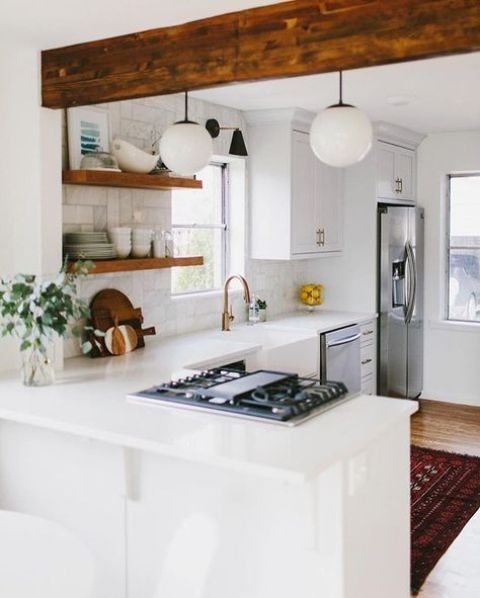 a white L-shaped kitchen spruced up with a wooden beam and shelves is very comfortable for cooking