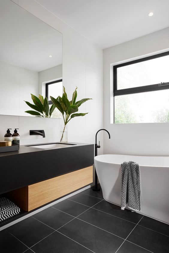 a modern space with a black framed window, dark tiles, a black and wood vanity and a tub
