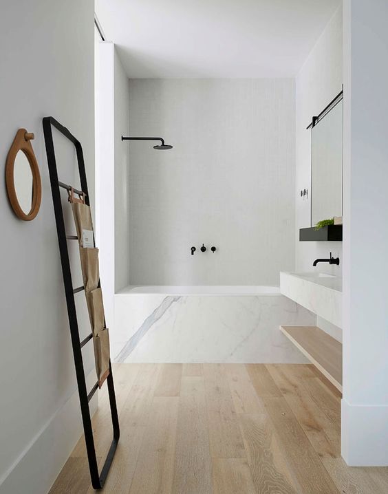 a simple elegant bathroom with wooden floors, a bathtub clad with marble and a marble vanity