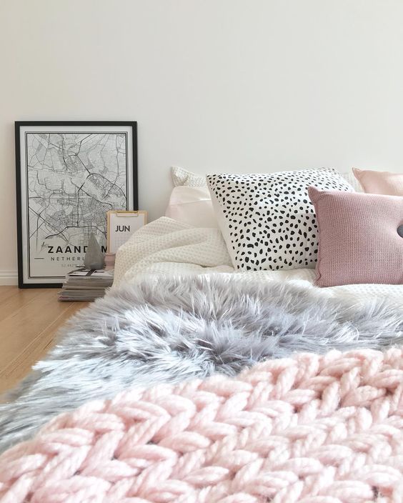 a cute girlish bed with a pink chunky knit throw, a faux fur grey blanket and creative printed pillows