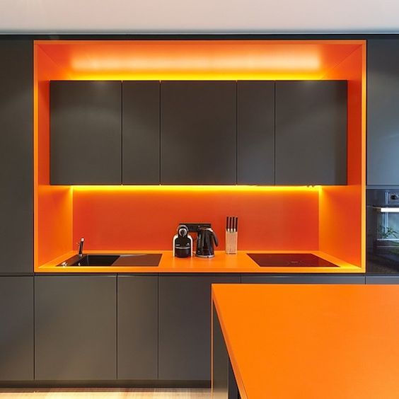 a minimalist grey kitchen with bold orange countertops, lights and a backsplash