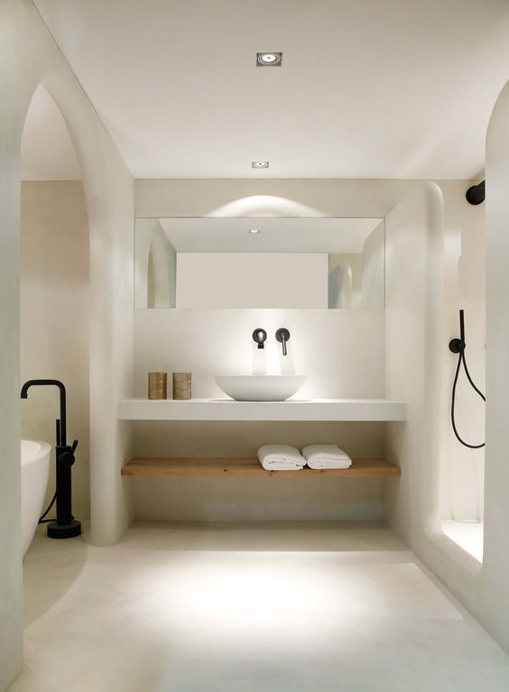 A neutral space decorated with light colored stone, a black faucet and a free standing tub and a vanity shelf