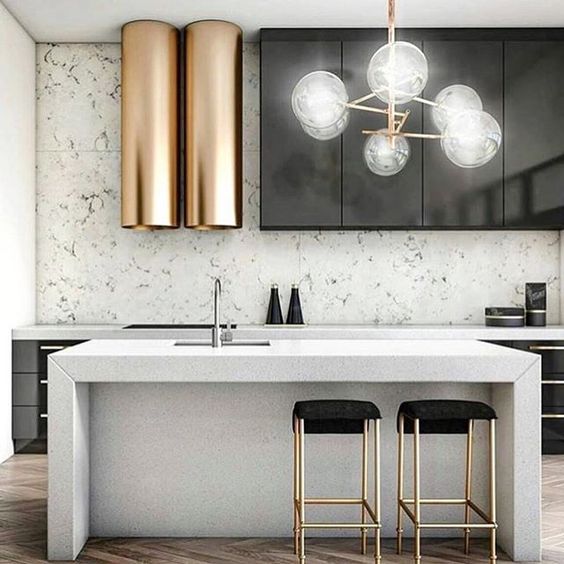a modern space with black metal cabinets, white stone counters and a backsplash and a unique brass hood