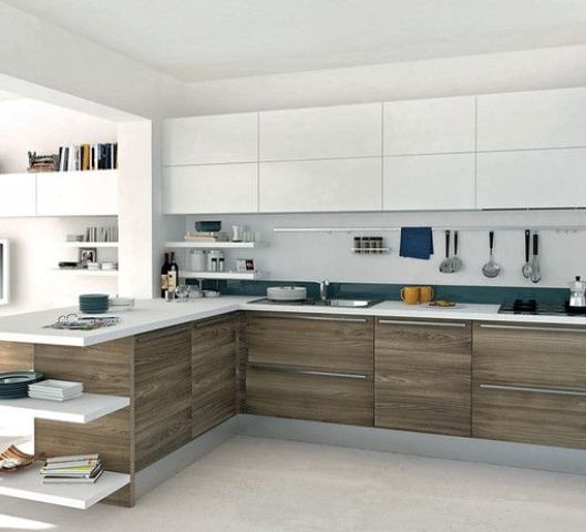 a bold white and wood L-shaped kitchen with teal touches and bookshelves to divide the spaces