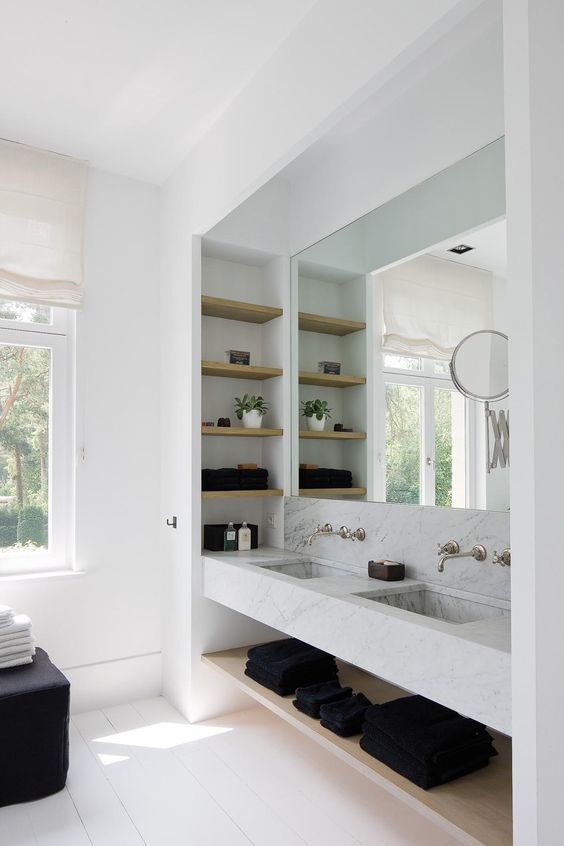 a functional sink space with white marble, wooden shelves and a large mirror
