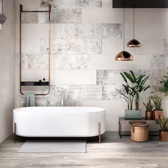 A chic modern space with neutral tiles, a free standing bathtub on copper legs, copper lamps and fixtures